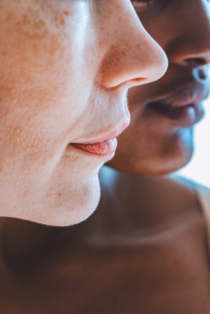 Nahaufnahme von zwei Personen, wobei der Fokus auf ihren Gesichtern im Profil liegt. Das Bild erfasst ihre Nasen, Münder und Teile ihrer Wangen und zeigt unterschiedliche Hauttöne. Der Hintergrund ist leicht unscharf.